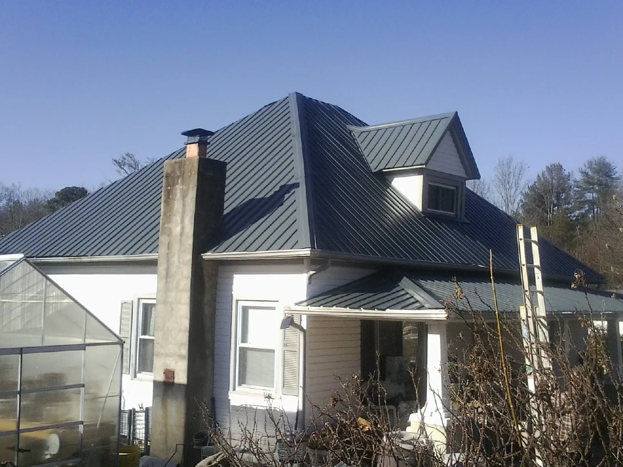Dark blue standing seam metal roof on a white farmhouse with dormer — Slate & Tile Roof Repair by Roofing Brothers in Ballwin