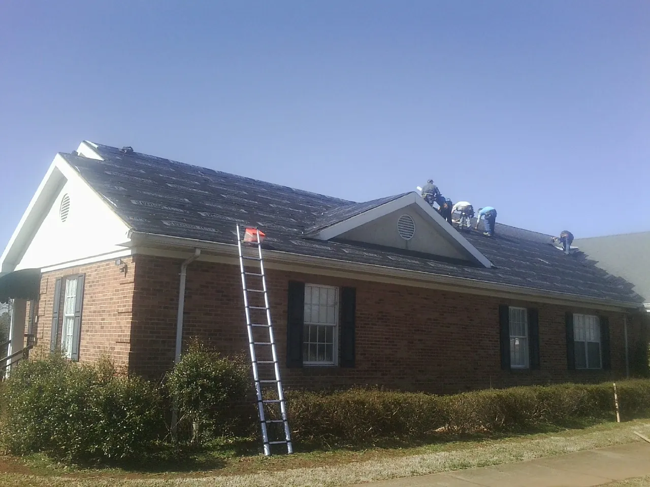 Crew tearing shingles off a brick ranch roof with a ladder set — Emergency Roof Repair work by our crew in Ballwin