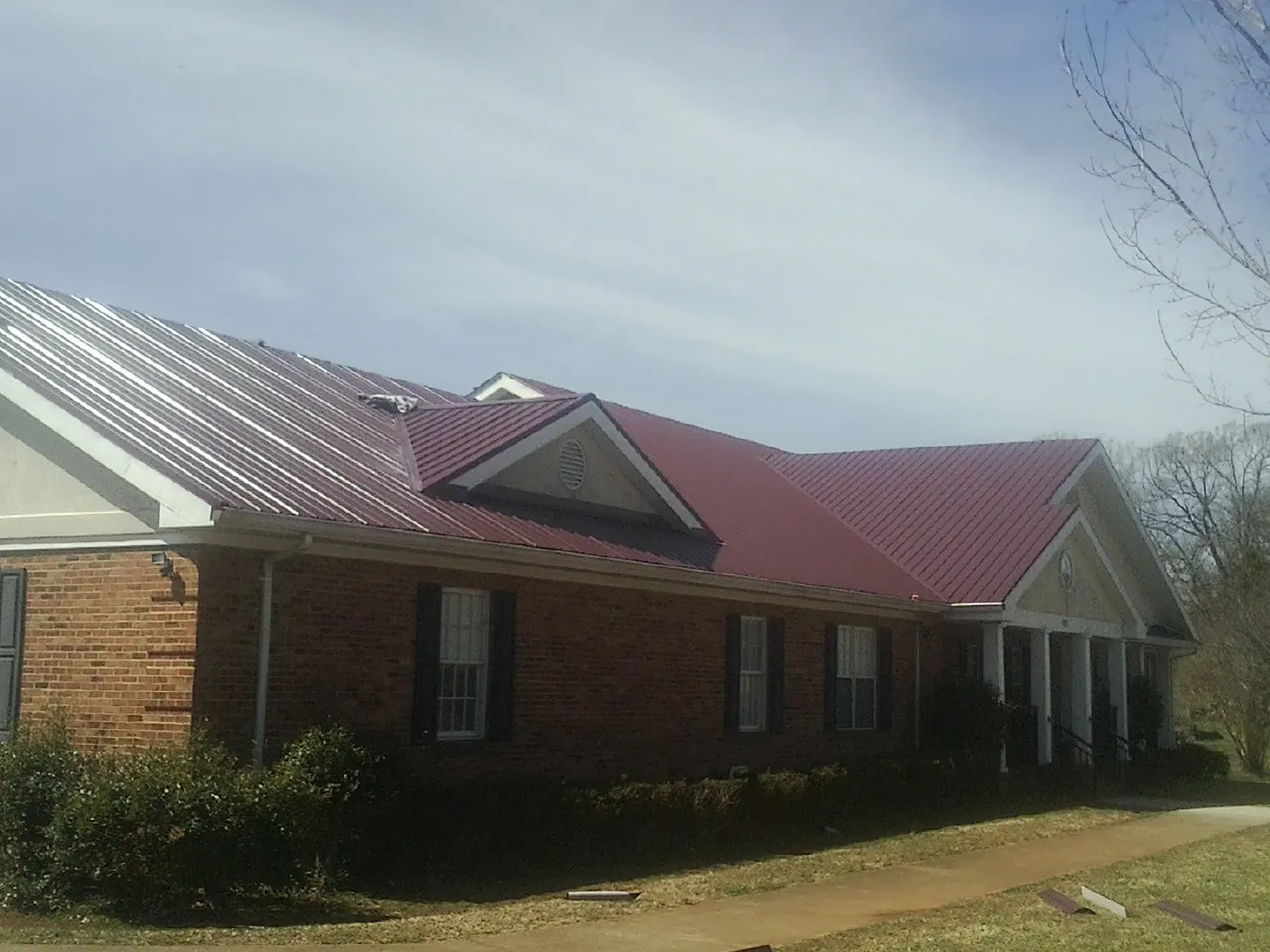 Red metal roof with gabled entries on a long brick building, from a Hail Damage Roof Repair job in Ballwin